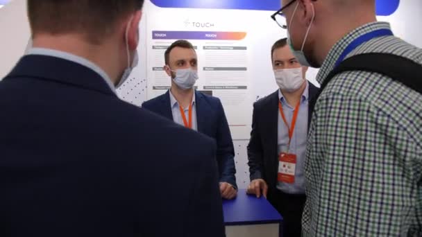 Employees in masks talk to visitors at business exhibition — стокове відео