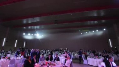 Misafirler yarı karanlık konser salonundaki masalarda yemek yiyorlar.