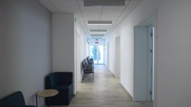 Metalik parlaklıkla çerçevelenmiş cam kapıya doğru uzun bir koridor uzanıyor. Deri kaplı koltuklar simetriyi ve sakin ritmi vurguluyor