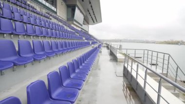 Mavi koltuklu uzun seyirciler bulutlu arka planda dururlar. Renkli düzenlemeli stadyum bölümü dinamik tasarımı vurguluyor