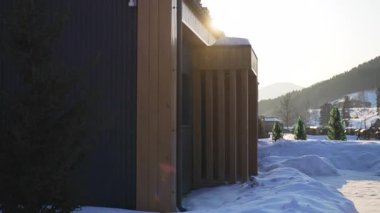 Kış alacakaranlığında karlı bahçede ahşap cepheli bir otel binası. Kayak merkezindeki misafirler için modern kamara. Ülke sahnesi
