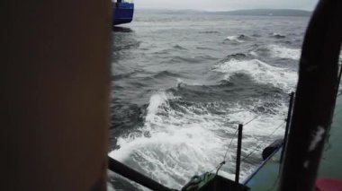 Büyük okyanus dalgaları kargo gemisinin etrafında ritmik olarak yükselip alçalıyorlar. Gemi güçlü rüzgar altında hafifçe eğildikçe, kamera yükselen suyu takip ediyor.