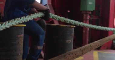 Tecrübeli denizci güverte boyunca kalın bir ip çeker. Kolları gergin ve kuvvetlidir. İnsan çelik gövde yanında demirleme hattını tutar. Yakınlarda titreyen dalgalar.