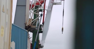 Yığılmış konteynırların üzerinde büyük vinç var. Metal sislerin içinde parlıyor. Ağır vinç kolları kargo ışıklarının üzerinde süzülür ıslak yüzeylerde titreşir