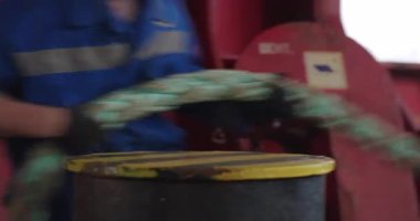 İşçiler, iskelenin yanında, kalın bir halat germe teknesiyle çekiyorlar. İp eldivenli ellerde kayar su altında parıldar