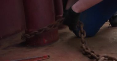 İşçiler ağır zincirleri kargo gemisinin masasına sıkıca bağlarlar. Denizci elleri demir demirleme teknesini iskeleye bağlıyor.