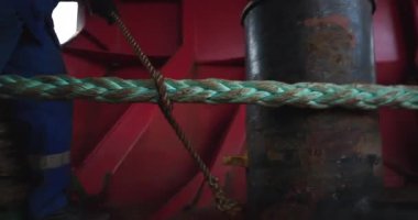Üniformalı işçi, gemi güvertesinde halata ince kablolar bağlıyor. Denizcilik sırasında demirleyen tankerleri bağlayan işçi kravatları