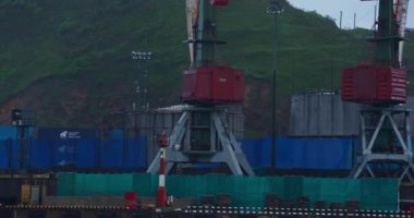 Yağmurlu bir günde deniz rıhtımında güçlü turnalar tepeye karşı. Dağın dibindeki sanayi limanında kargo taşımacılığı için ekipman