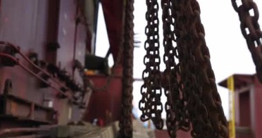 Rüzgarda sallanan eski metal zincirler konteynır tarafında asılı duruyor. Büyük deniz tanker güvertesinde kargo bağlama ve taşıma ekipmanları
