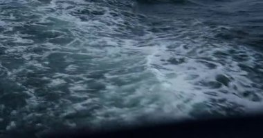 Köpüklü gök mavisi deniz kenarındaki sürat teknesinin arkasında yuvarlanıyor. Okyanus dalgaları ve sıçramalar kaba yüzeyde soyut desenler oluşturur.