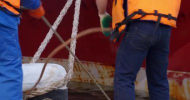 Rıhtım işçisi ıslak beton iskele boyunca demirleme halatlarını çekiyor. Endüstriyel uyum çelik gerilimi ve deniz durgunluğu arasında yayılır.