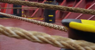 İpler ve ağır çapa zinciri ıslak çelik güvertede gri deniz ışığı altında parlıyor. Sahne güç ve dayanıklılık soluyor.