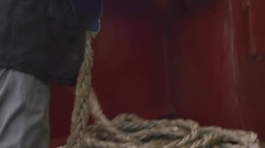 Denizciler ıslak güvertede halat bükerler. Elleri tuzlu su ile parlar. Takım çalışması. Ekip halatı ve senkronize işçilik deniz havasını doldurur.