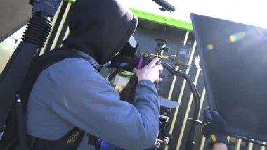 ALMATY, KAZAKHSTAN - 28 Eylül 2025: Kapüşonlu kameraman stüdyoda modern kamerayla film sahneleri çekiyor. Çekim ekibi, köşkte kamera ve dijital ekipman kullanıyor.