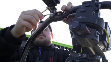ALMATY, KAZAKHSTAN - 28 Eylül 2025: sakallı kameraman fiş cihazı film setindeki kameraya. Yetenekli operatör dış mekanda video kayıt cihazları hazırlıyor.