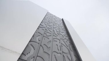 Cilalı metal panellerle kaplı ön duvar ışığı yansıtıyor ve dekoratif desenler çarpıcı bir yüzey oluşturuyor. Bina modern bir anlam ifade ediyor.