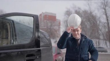 ALMATY, KAZAKHSTAN - 07 Aralık 2025: adam kasket kapısının yanında gururla gülümseyerek durur. İşçi başlığı başlığa yerleştirir. Sabah vardiyası için hazırlama araçları dikkatlice yerleştirilir.