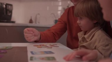 ALMATY, KAZAKHSTAN - 07 Aralık 2025: Kadın evdeki masada zar atan çocukla masa oyunu oynuyor. Genç kadın, sırayla oyun masasında mavi zarlar atıyor.