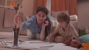 ALMATY, KAZAKHSTAN - 07 Mayıs 2025: genç kadın kanepede çocukla birlikte resim çiziyor. Küçük çocuk yanında oturup çizim yaparken, kadın elinde kalem tutarak büyük kağıtlara resim çiziyor.