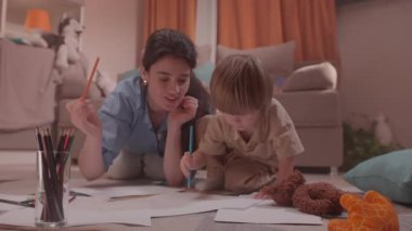 ALMATY, KAZAKHSTAN - Mayıs 07 2025: Erkek, kadın yerde izlerken turuncu kalemle resim çiziyor. Erkek, kadın kâğıdı sabitlerken yol gösterirken öne doğru eğilir.