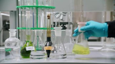 Eldivenli el, sarı matarayı seçiyor. Sonra da raftan cam değiştiriyor. Laboratuvar teknisyeni yakıt örneklerini karşılaştırdı.