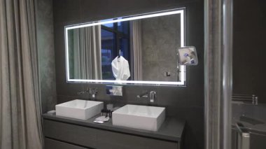 Otel banyosunda geniş lavabo alanı geniş ayna ve düzgün yerleştirilmiş hijyen şişeleri var. Işıl ışıl iç mekan birinci sınıf bakımı vurguluyor