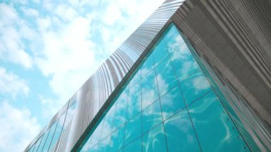 Düşük açılı çerçeve, turkuaz cam cephe ve metal çatının keskin köşesini oluşturuyor. Mavi gökyüzü arkaplanı doldururken paneller ışıkla parıldıyor