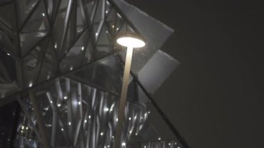 Sokak lambası modern tiyatronun yakınında gece havada süzülen küçük kar parçacıklarını ön plana çıkarıyor. İnce bir parıltı barışçıl atmosferik bir an yaratır.