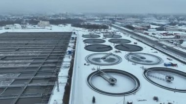 Karla kaplı arıtma tesisinde birden fazla yuvarlak havacılık ve yerleşim havuzu bulunuyor. Geometrik ritim soğuk sanayi arazisine hakim.