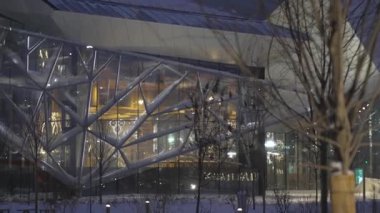 Dekoratif cam cepheli tiyatro binası akşam saatlerinde parlıyor. Şeffaf yüzeyler şehir ışıklarını yansıtıyor