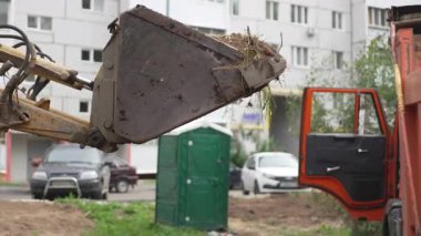 Toprak ve kuru otlarla dolu ağır kazıcı kovası kamyon yatağına doğru yavaşça ilerliyor. Ağır makineler kesin inşaat görevini yerine getiriyor