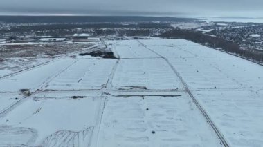 Minimum kış manzarası sonsuz beyaz zemin ve uzak şehir hatlarını gösteriyor. Bunaltıcı bulutlu gökyüzü duygusal olarak ağır tonu güçlendirir