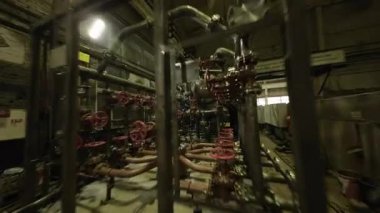 ALMATY, KAZAKHSTAN - 18 Eylül 2025: Endüstriyel atölye içindeki yoğun birbirine bağlı boru hatlarından kamera süzülüyor. Pürüzsüz hareket labirent mühendislik yapısını vurguluyor