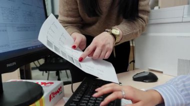 ALMATY, KAZAKHSTAN - 26 HAZİRAN 2026: Kadın yönetici bilgisayar klavyesinde yazı yazan meslektaşlarına kağıtları gösteriyor. Şirket çalışanları ofis işyerindeki mali verileri kontrol ederler