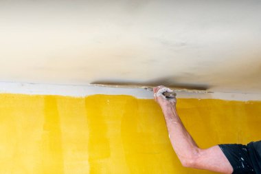 Yakın plan. Müteahhit işçilerin el boşlukları tavanda macun sıva ile kaplanmış spatula ile hizalanır. Yenileme ve inşaat çalışmaları 