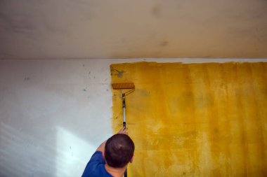 İnşaat alanındaki işçiler, duvarlara sarı astar astar yapıştırıyor. Yenileme konsepti