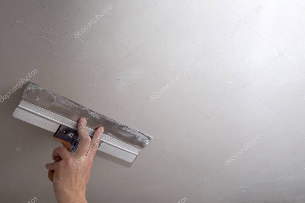 Hand of builder worker spacks ceiling with putty plaster aligning ceiling with spatula. Renovation and construction works