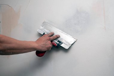 Müteahhit işçilerin eli duvarları macun alçısıyla kaplıyor. Duvarı spatulayla hizalıyor. Yenileme ve inşaat çalışmaları