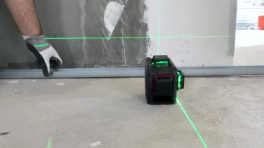 İnşaat işçisi inşaat sahasında daha fazla ölçüm için modern lazer seviyesini ayarlıyor, yeşil ışınları doğru ölçümler için gösteren inşaat aleti