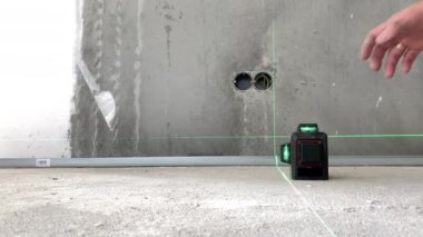 İnşaat işçisi inşaat sahasında daha fazla ölçüm için modern lazer seviyesini ayarlıyor, yeşil ışınları doğru ölçümler için gösteren inşaat aleti