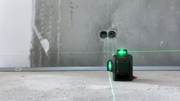 さらに測定するための建設現場の床に近代的なレーザーレベルを設定する建築労働者 正確な測定を取るための緑の光線の十字線を示す建設装置 — ストック動画