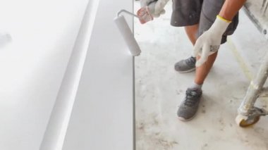 İşteki ressam ahşap kapıyı beyaz boyayla boyuyor.