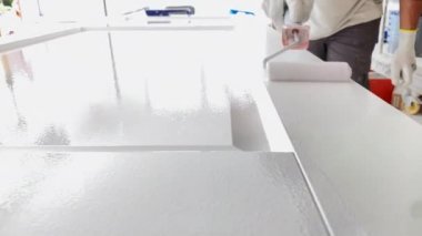 İşteki ressam ahşap kapıyı boya rulosuyla beyaz boyayla boyuyor. Profesyonel resim hizmetleri