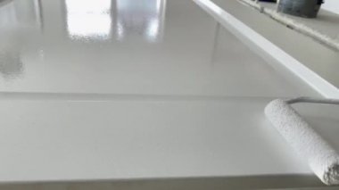 İşteki ressam ahşap kapıyı boya rulosuyla beyaz boyayla boyuyor. Profesyonel resim hizmetleri