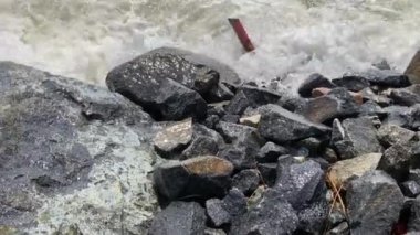 Su sıçratan deniz dalgaları ve köpükler kayalık kıyıya çarpıyor.