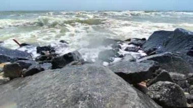 Su sıçratan deniz dalgaları ve köpükler kayalık kıyıya çarpıyor. 