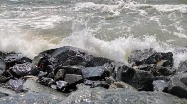 Su sıçratan deniz dalgaları ve köpükler kayalık kıyıya çarpıyor.