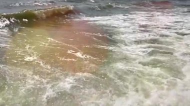 Su sıçratan deniz dalgaları ve köpükler kayalık kıyıya çarpıyor.