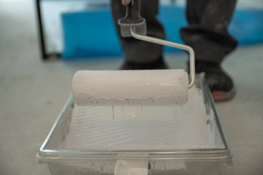 Plastiğin üzerine beyaz boya batırılmış bir boya silindirinin yakın çekimi. 