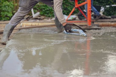 Bir inşaat işçisinin diz çöküp yeni ıslak betonu el küreğiyle dümdüz etmesine yakın çekim. İnşaat alanında çimento bitirme, döşeme işi